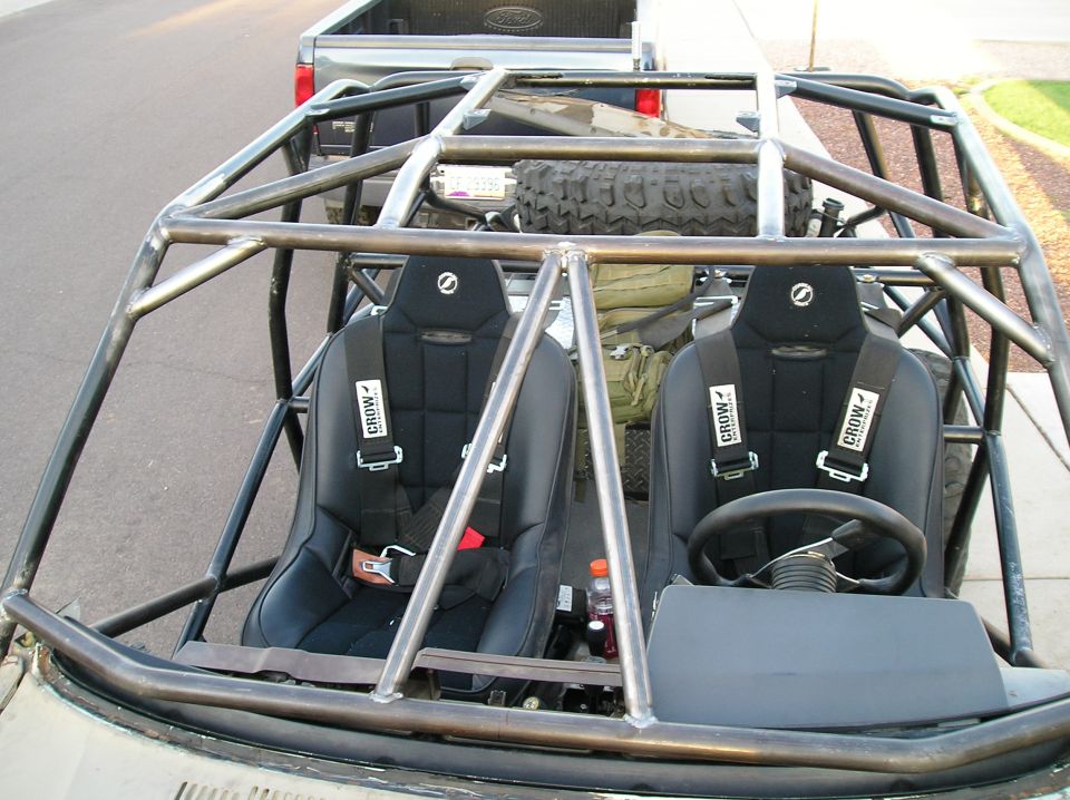 Custom off-road vehicle interior with roll cage, two black racing seats with Crow harnesses, and a spare tire visible behind the seats