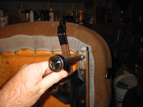 1988 Ford Bronco - A hand holds a socket wrench on a mounting bolt at the corner of an upside-down brown cloth bucket seat, with the black seat rail bracket a…