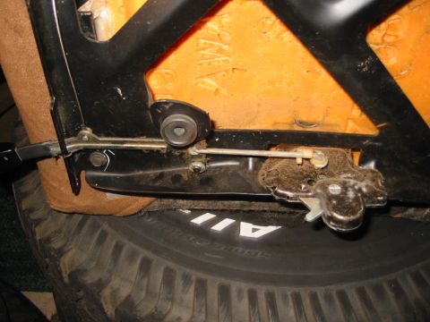 1988 Ford Bronco - Close-up of the underside of a bucket seat turned upside down on a tire, showing the black tubular seat-back frame, orange foam, the tilt/r…