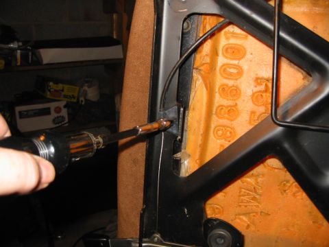 1988 Ford Bronco - A screwdriver tip works at the cable attachment point on the black tubular seat-back frame of an inverted bucket seat, with orange foam sta…
