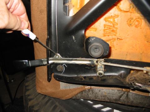 1988 Ford Bronco - A hand uses a small screwdriver to pry the tilt-release cable end off its lever on the underside of a bucket seat frame, with the black tub…