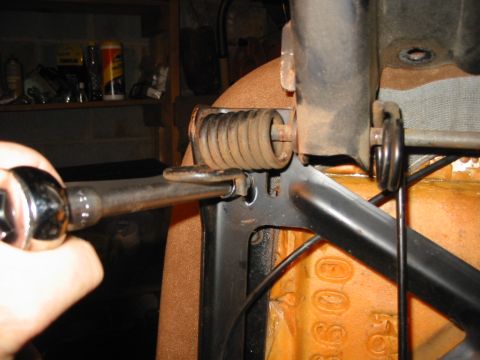 1988 Ford Bronco - A hand works a socket wrench on a corner mounting bolt of a bucket seat frame, with the seat inverted in a garage to expose the coil return…