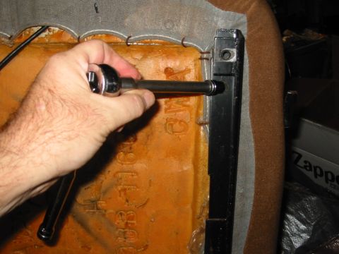 1988 Ford Bronco - A hand works a socket on a long extension to reach a bolt in the black steel seat rail bracket along the edge of a seat back, with the brow…