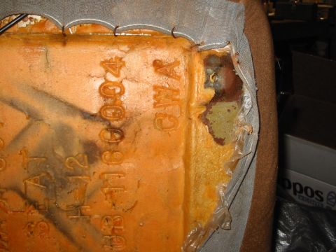 1988 Ford Bronco - Close-up of the underside corner of a removed bucket seat cushion with the fabric trim cover peeled back, exposing molded orange foam stamp…