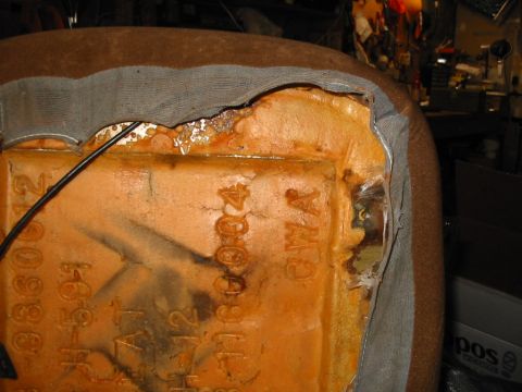 1988 Ford Bronco - Back side of a seat back with the brown cloth cover and gray backing peeled away, exposing the molded orange foam cushion with cast-in part…