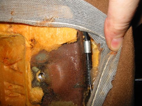 1988 Ford Bronco - A hand pulls back the gray scrim and brown upholstery on a seat back to expose the orange foam, a rusty stamped-steel seat frame panel with…