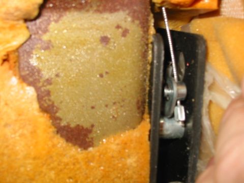 1988 Ford Bronco - Extreme close-up inside a disassembled seat back, showing crumbling orange-tan foam padding with a discolored patch and a black plastic tri…