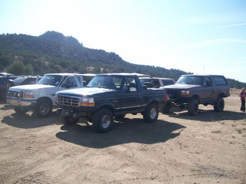 1993 Ford Bronco - A lineup of Ford Broncos, including a dark blue model with off-road modifications, parked outdoors.