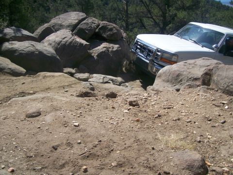 1993 Ford Bronco - A white pickup truck maneuvers through a challenging rocky terrain with large boulders on either side.
