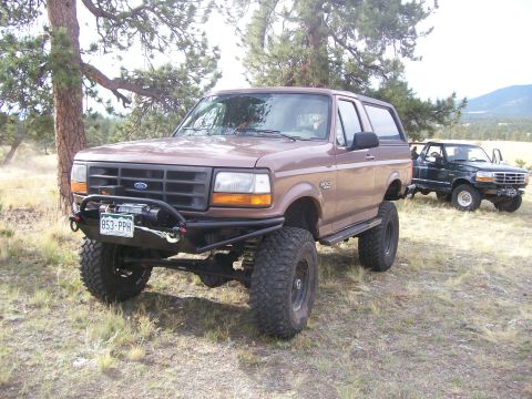 1993 Ford Bronco - Two Ford Broncos are parked off-road in a grassy, wooded area.