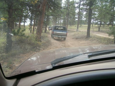 1993 Ford Bronco - A line of vehicles navigates a dusty trail surrounded by pine trees.