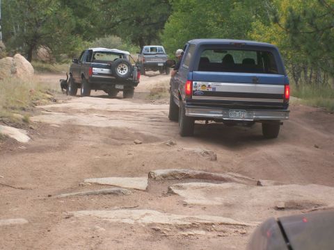 1993 Ford Bronco - A blue 1992 Ford Bronco navigates a challenging rocky terrain on a dirt road, followed by other vehicles.