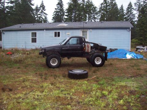 1985 Toyota Pickup/SR5 - This modified 1985 Toyota Pickup features oversized tires and a custom flatbed, parked in a grassy yard.