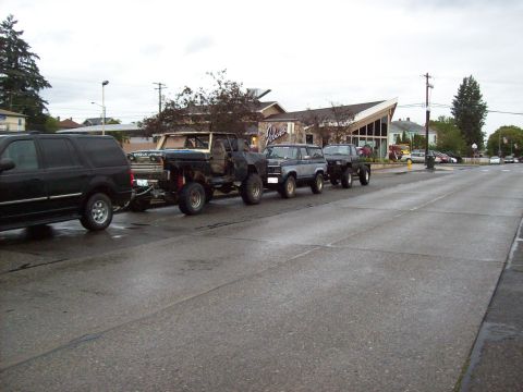 1985 Toyota Pickup/SR5 - A convoy of off-road vehicles travels down a street on a cloudy day.