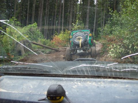 1985 Toyota Pickup/SR5 - A green off-road vehicle navigates a muddy trail through a dense forest.