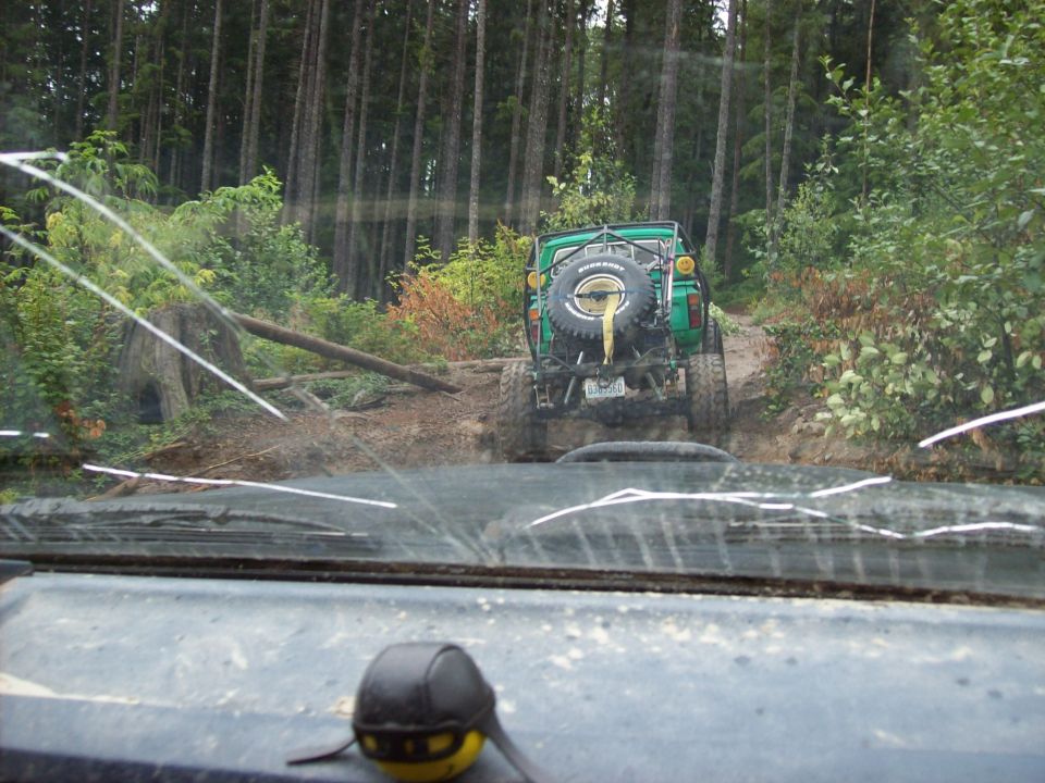 Green off-road vehicle with spare tire on back driving on a dirt path in a forest