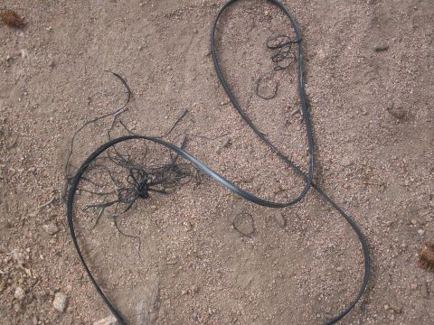 1993 Ford Bronco - A mess of black cables lies tangled on a dirt and gravel surface.