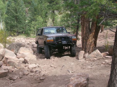 1993 Ford Bronco - Modified 1993 Ford Bronco tackling a challenging rocky path in a wooded area.