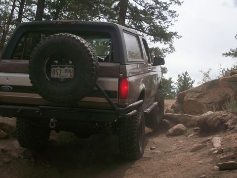 1993 Ford Bronco - Ford Bronco navigates a rocky off-road path, spare tire visible on the rear.