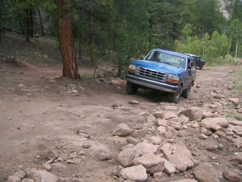 1993 Ford Bronco - A blue Ford F-150 navigates a rough, rocky off-road trail.