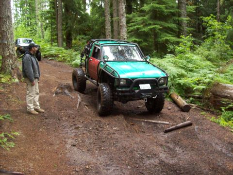 1985 Toyota Pickup/SR5 - A modified Toyota pickup truck navigates a forest trail with another vehicle visible in the background.