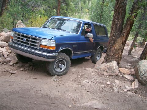 1993 Ford Bronco - This blue 1993 Ford Bronco is shown tackling a challenging off-road path with rocky terrain.