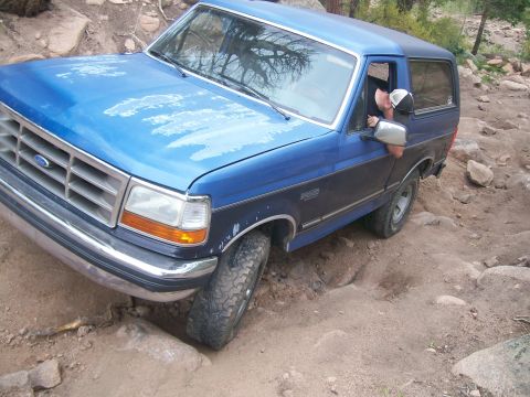 1993 Ford Bronco - Blue Ford Bronco struggling on a steep, rocky off-road path.