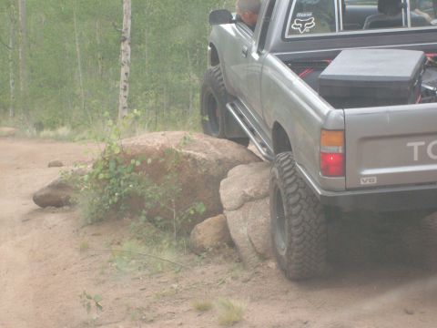 1993 Ford Bronco - A silver Toyota pickup truck is shown off-roading over large rocks.