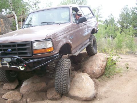 1993 Ford Bronco - A driver navigates a Ford Bronco over a rocky obstacle on an outdoor trail.