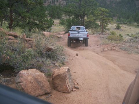 1993 Ford Bronco - A Toyota pickup truck navigates a , off-road path surrounded by trees and boulders.