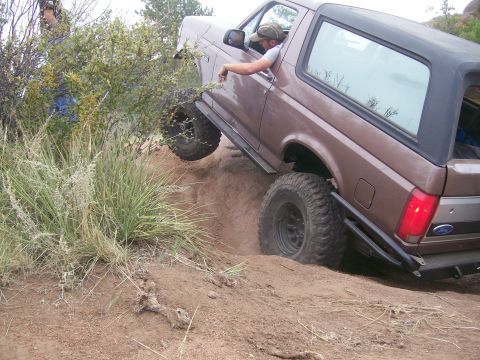 1993 Ford Bronco - Brown Ford Bronco navigates a steep dirt incline with its front right tire partially stuck.