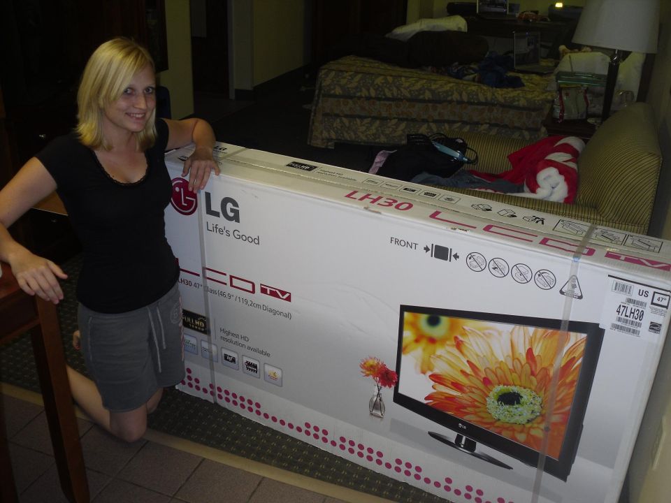 Woman kneeling next to a large LG LH30 LCD TV box. Box shows a picture of the TV screen with flowers