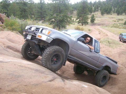 1993 Ford Bronco - Off-road Toyota pickup truck navigating a rocky trail with a second vehicle in the distance.