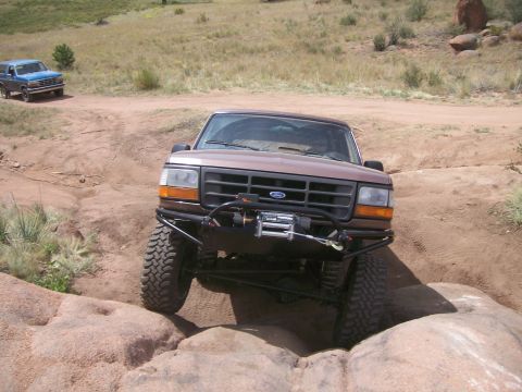 1993 Ford Bronco - A brown Ford Bronco tackles a challenging off-road course with another blue SUV in the background.
