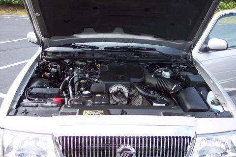 2001 Ford Crown Victoria - The engine bay of a silver 2004 Mercury Grand Marquis is visible with the hood raised, revealing the V8 engine and associated parts.