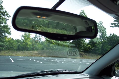 2001 Ford Crown Victoria - View from inside a vehicle, looking through the windshield at trees and a parking lot, with the rearview mirror prominent.