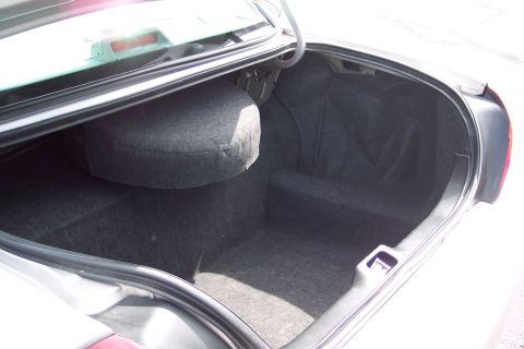2001 Ford Crown Victoria - The open trunk of a car reveals a spare tire and the carpeted interior space.