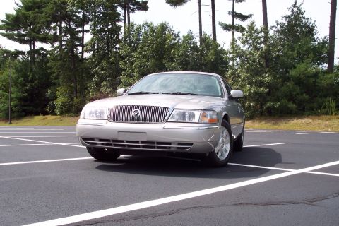 2001 Ford Crown Victoria - A silver 2004 Mercury Grand Marquis is parked in a lot with trees in the background.