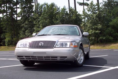 2001 Ford Crown Victoria - Front view of a silver Mercury Grand Marquis parked in a lot with trees in the background.