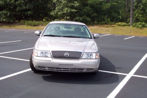 2001 Ford Crown Victoria - A silver Mercury Grand Marquis is parked in a lot with trees in the background.