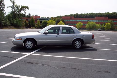 2001 Ford Crown Victoria - A silver sedan is parked in an empty parking lot with a building in the background.