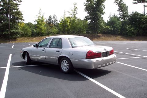 2001 Ford Crown Victoria - Silver 2004 Mercury Grand Marquis parked in a lot, viewed from the rear three-quarter angle.