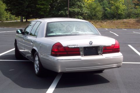 2001 Ford Crown Victoria - Silver Mercury Grand Marquis LS sedan parked in a lot with trees in the background.