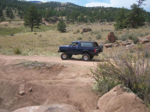 1993 Ford Bronco - This blue 1993 Ford Bronco is captured mid-drive on a dusty trail, navigating a , rocky landscape.