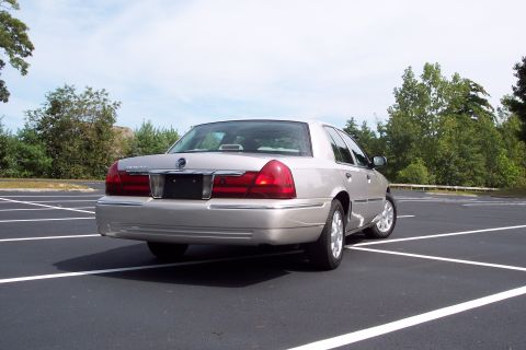 2001 Ford Crown Victoria - Silver Mercury Grand Marquis parked in a lot with trees in the background.