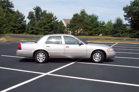 2001 Ford Crown Victoria - A silver sedan is parked in a lot with white lines marking parking spaces.