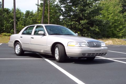 2001 Ford Crown Victoria - A silver sedan is parked in an empty lot with trees in the background.