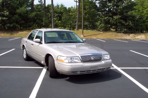 2001 Ford Crown Victoria - This silver sedan, identified as a 2004 Mercury Grand Marquis, is parked in a lot with trees in the background.