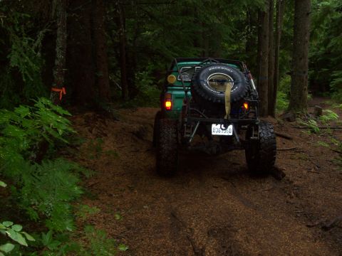 1985 Toyota Pickup/SR5 - A modified pickup truck navigates a muddy trail through a dense forest.