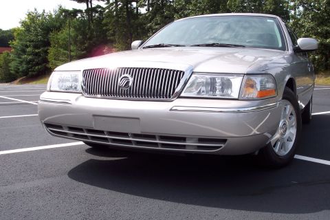 2001 Ford Crown Victoria - Silver sedan with a prominent chrome grille and headlights is parked in a lot.